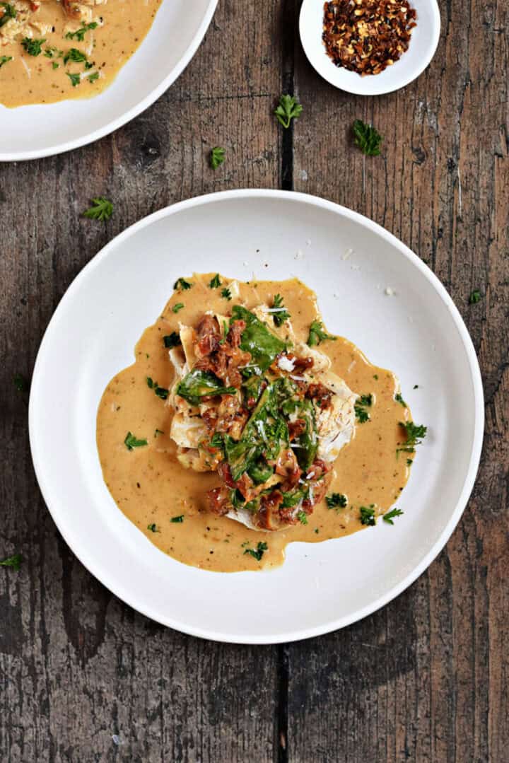 Chicken breast topped with sun-dried tomatoes, spinach, and creamy sauce in a shallow bowl.
