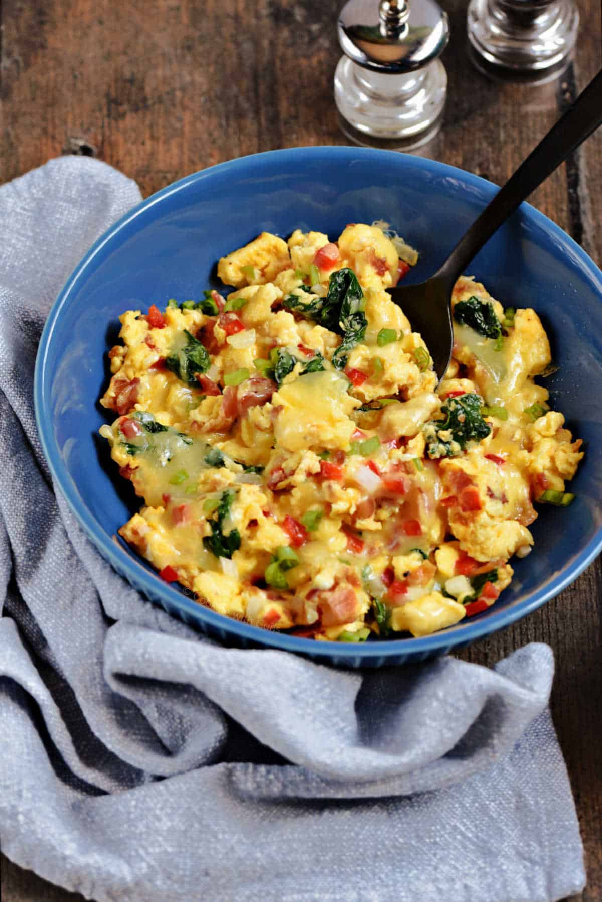 Scrambled eggs with diced red pepper, onion, and spinach in a serving bowl.