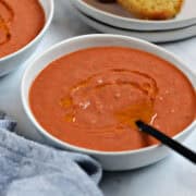 A bowl of bright orange gazpacho soup drizzled with olive oil.