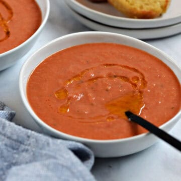 A bowl of bright orange gazpacho soup drizzled with olive oil.