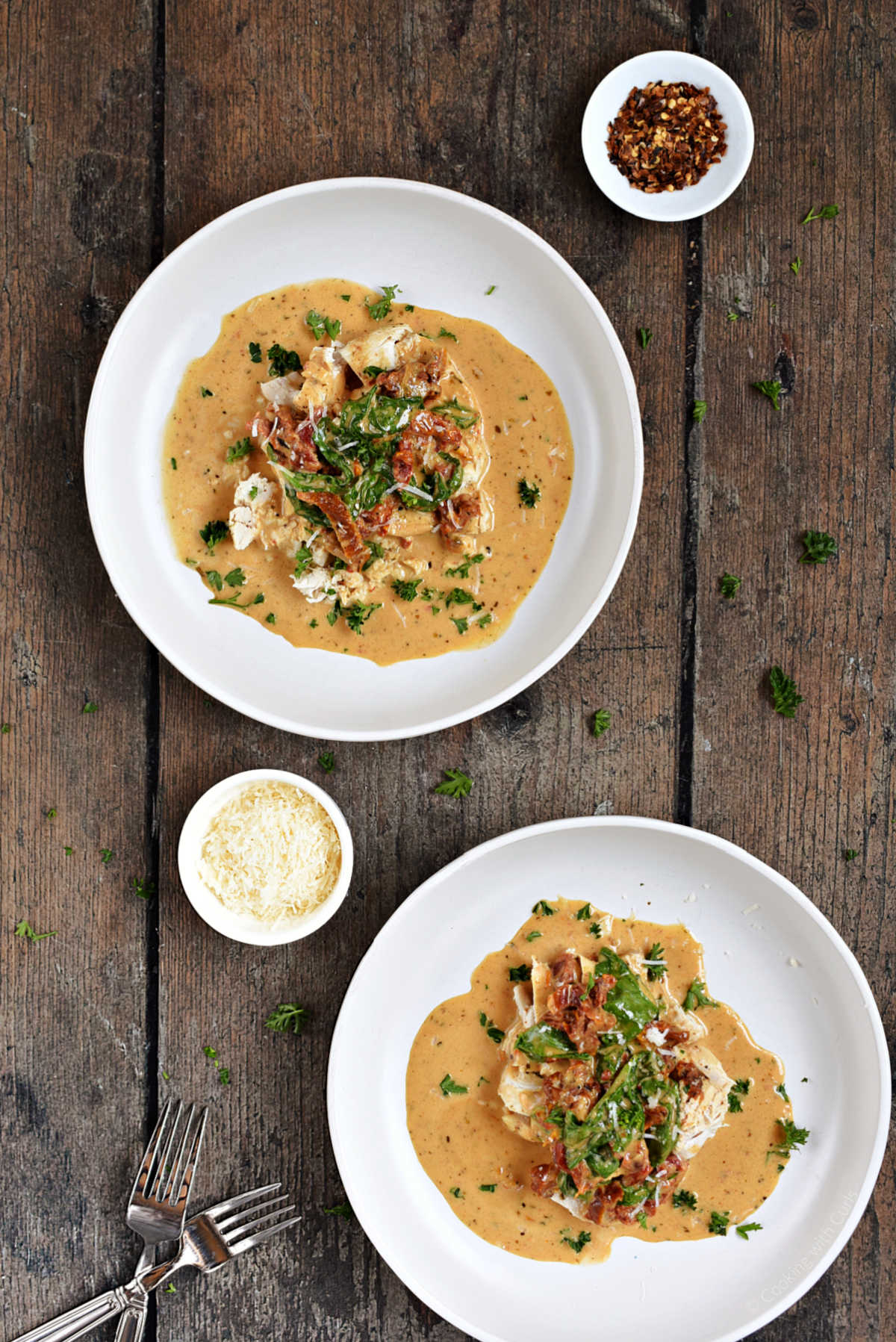 Two bowls of Instant Pot Tuscan chicken sprinkled with parmesan cheese and chopped parsley.