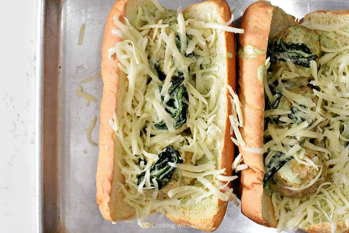 Meatball sandwiches toped with grated mozzarella cheese and green Alfredo sauce.