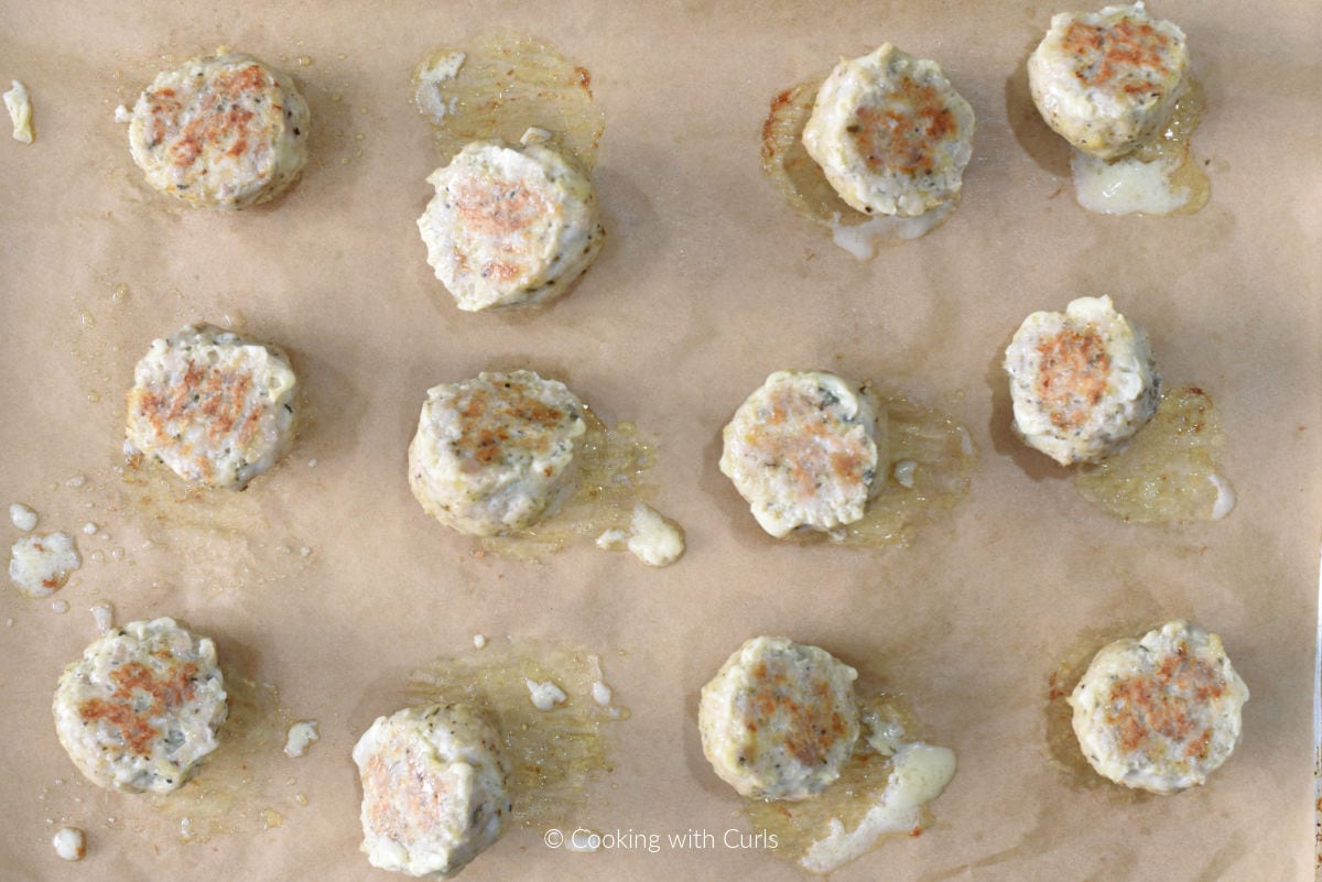 Twelve cooked chicken meatballs on parchment lined baking sheet.
