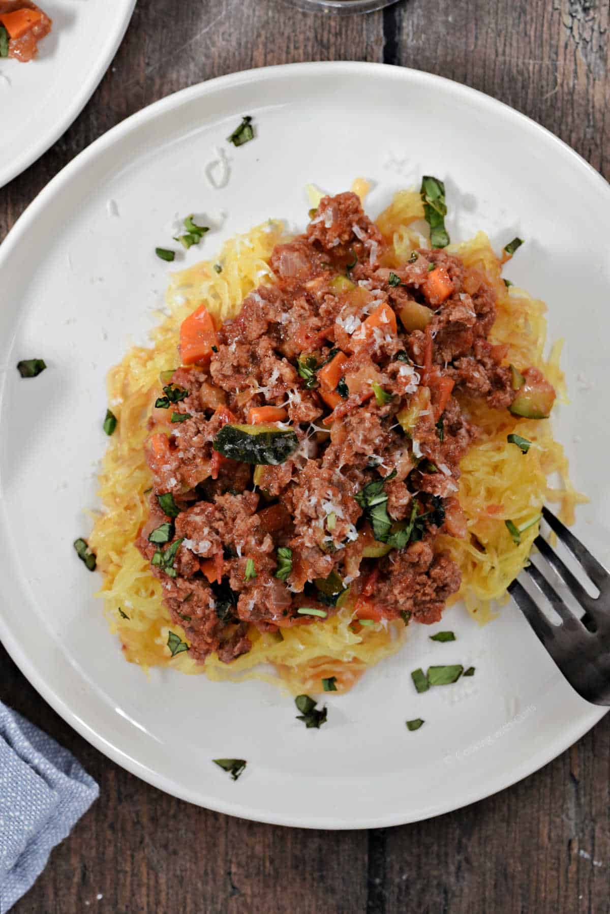 A plate of spaghetti squash strands topped with meat sauce and grated parmesan cheese.