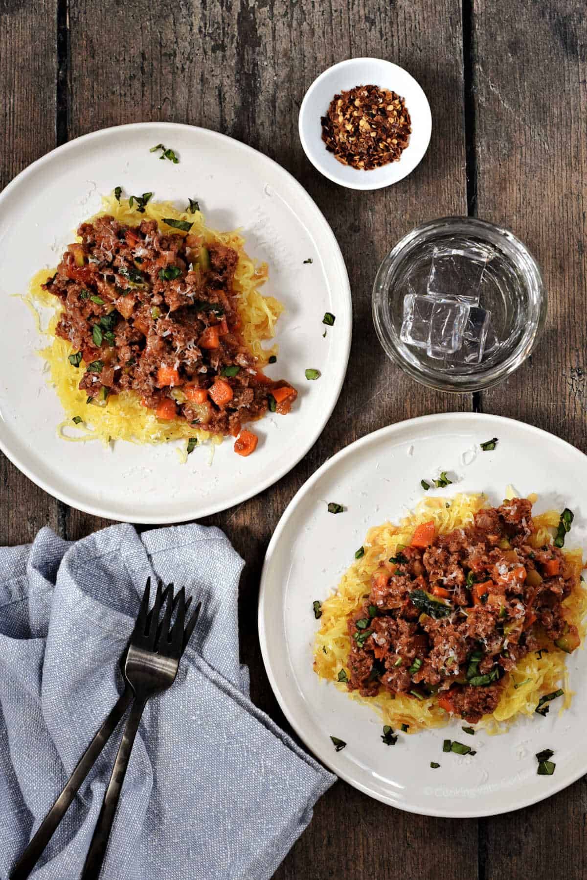 Two plate with spaghetti squash threads topped with meat sauce and chopped parsley.