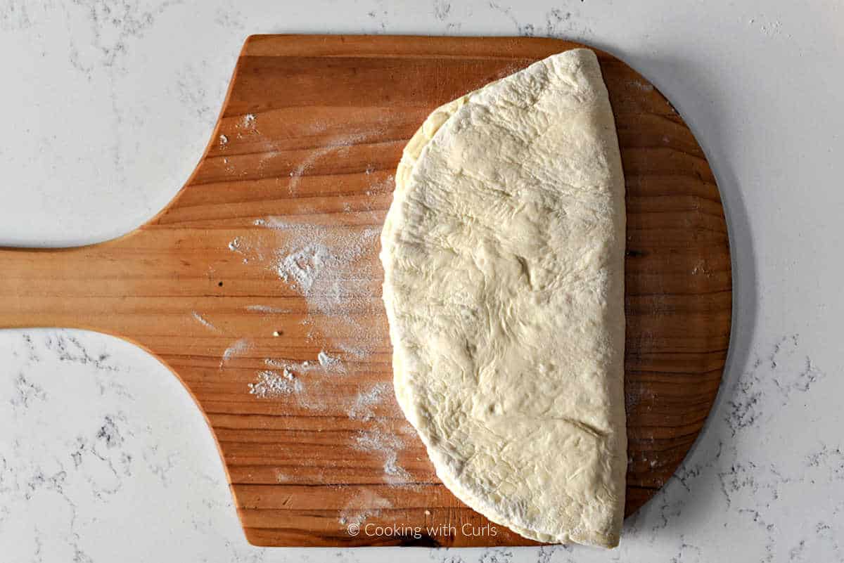 Folded pizza dough on wooden pizza peel.