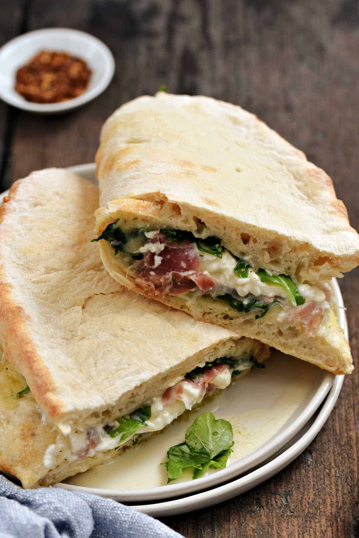 Folded pizza sandwich with prosciutto, arugula, and mozzarella cheese on a small plate.