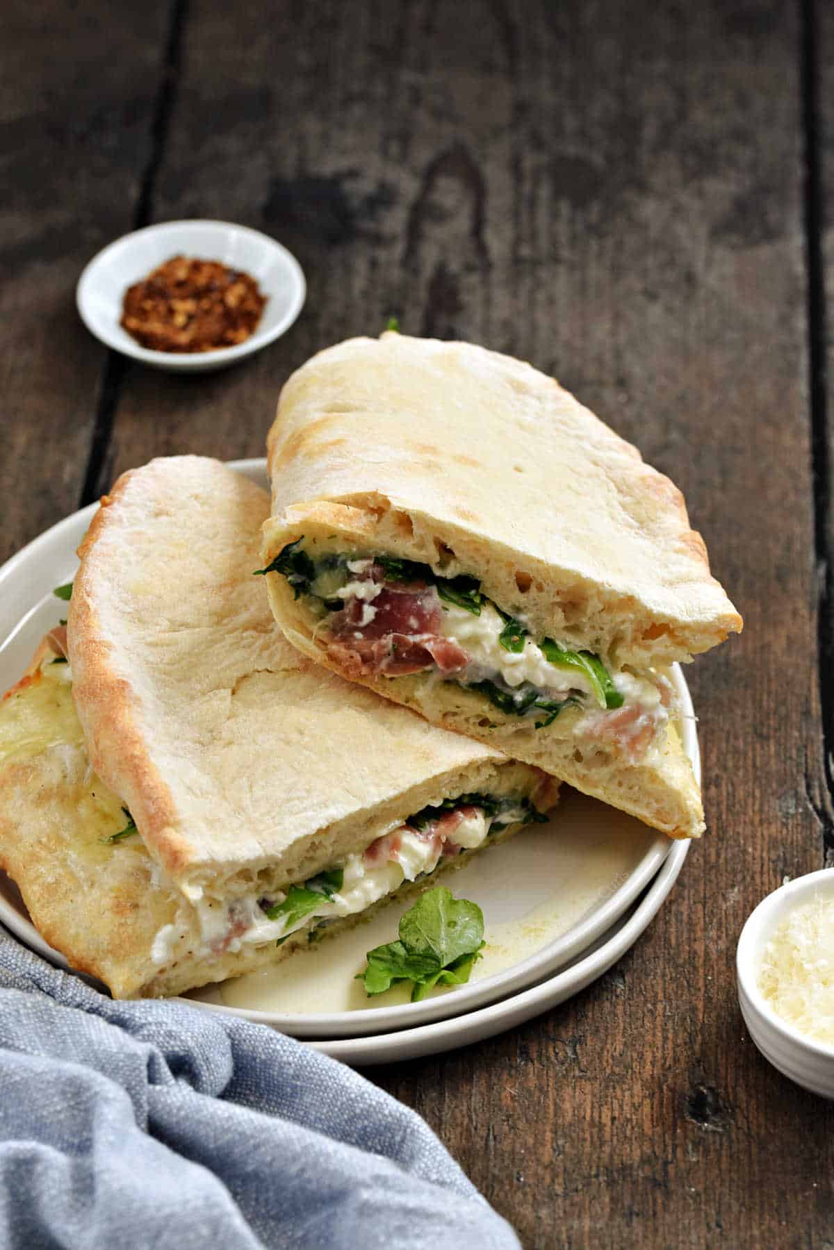 Pizza crust wrapped around arugula, melted mozzarella, and prosciutto cut in half and stacked on a plate.