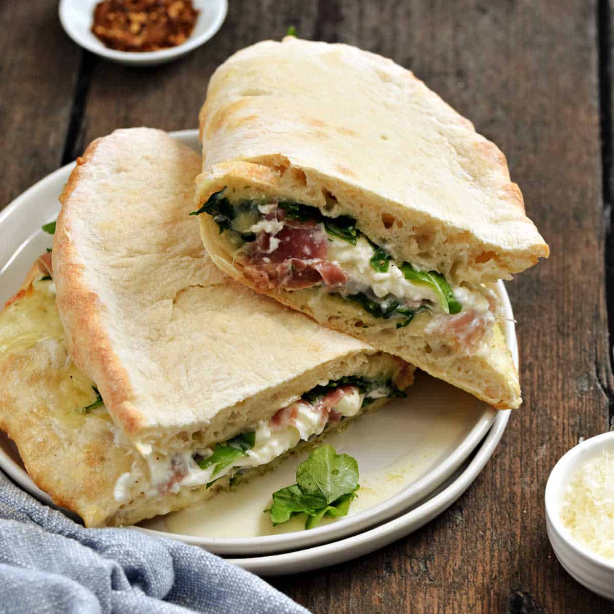 Pizza crust wrapped around arugula, melted mozzarella, and prosciutto cut in half and stacked on a plate.