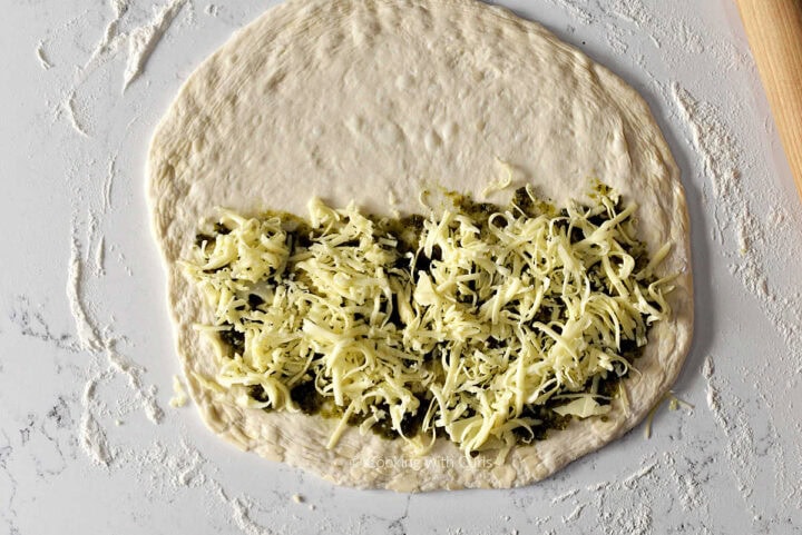 Pizza dough circle topped with pesto and mozzarella cheese.