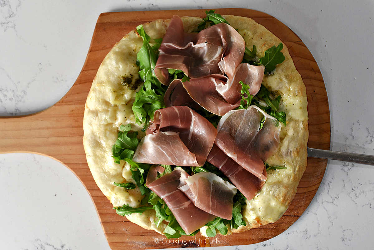 Prosciutto, arugula, and pesto on pizza crust.