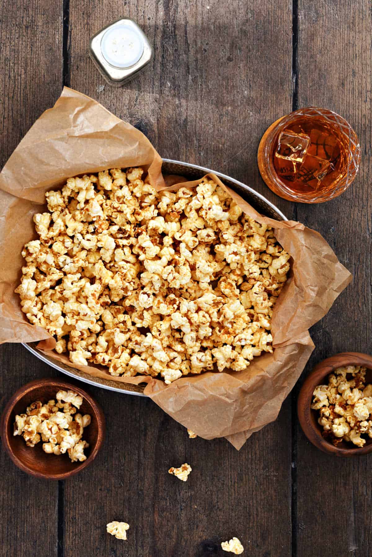 Buffalo seasoned popcorn in a parchment lined metal basket with cocktail in the background.