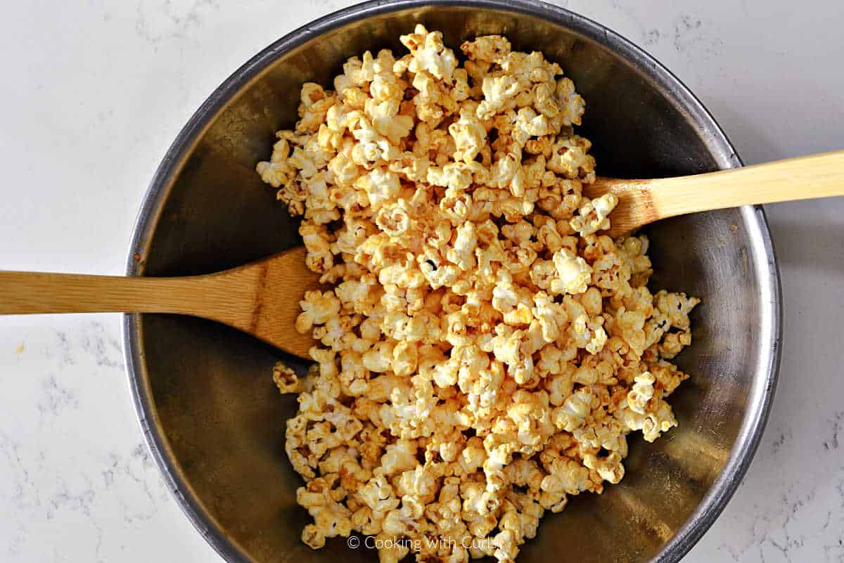Popcorn tossed in a mixing bowl with buffalo sauce mixture.