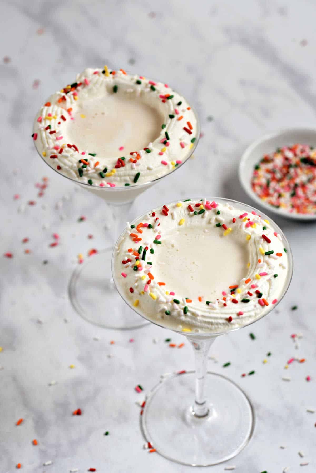 Two creamy white drinks with whipped cream and sprinkles in martini glasses.