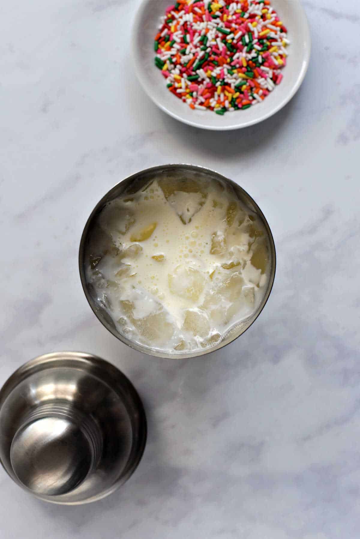 Birthday cake martini ingredients in cocktail shaker with ice.