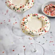 Two creamy white drinks with whipped cream and sprinkles in martini glasses.