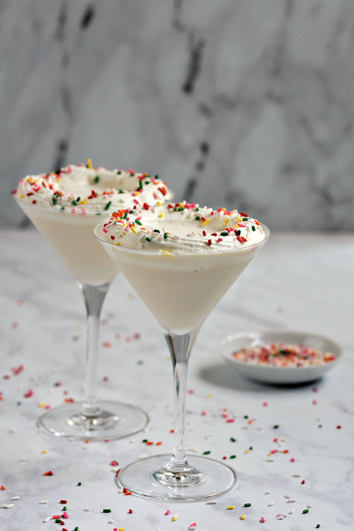 Two creamy white drinks with whipped cream and sprinkles in martini glasses.