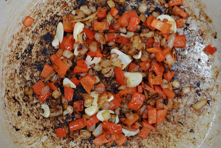 Chopped onion, red pepper, and sliced garlic cooking in skillet.