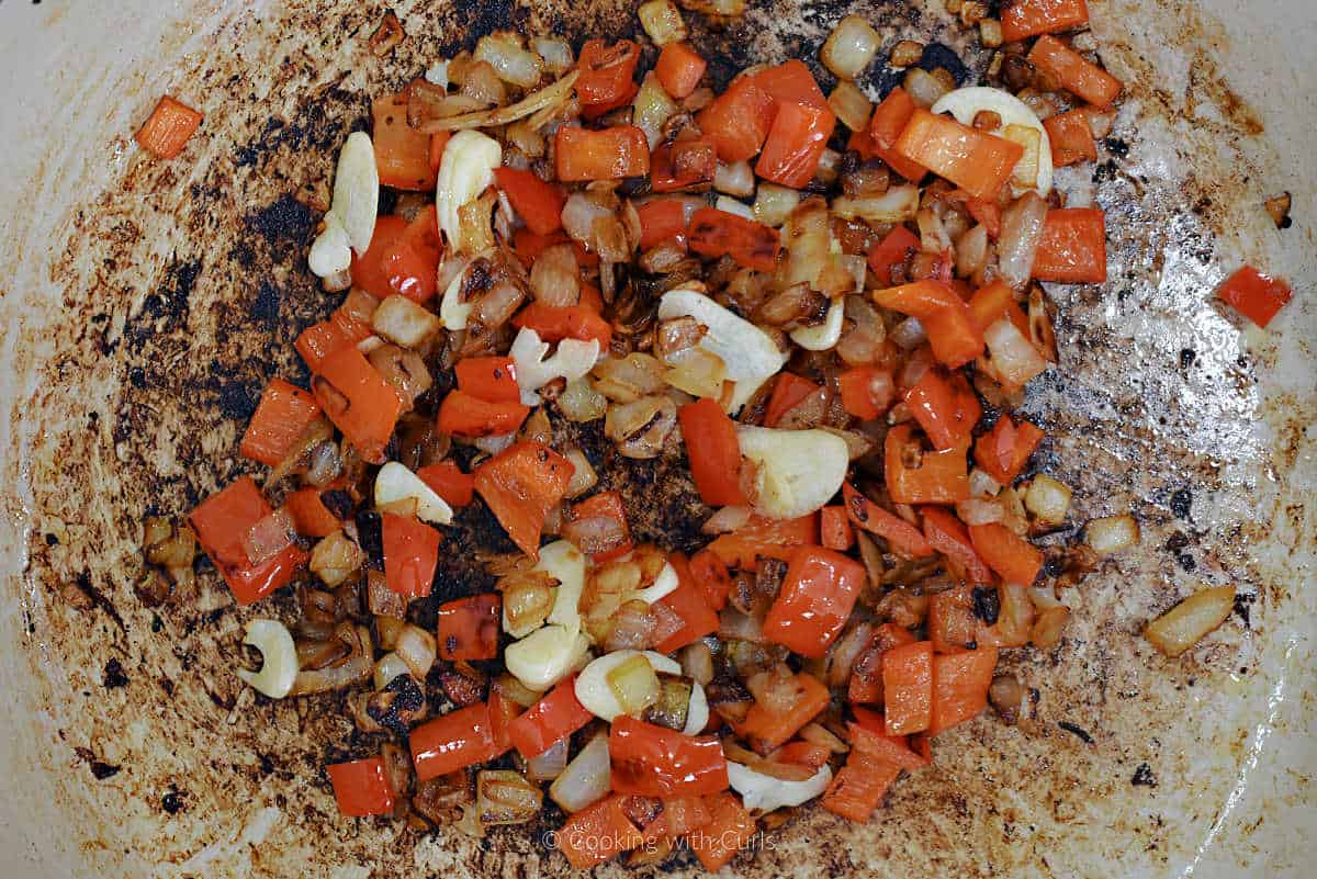 Chopped onion, red pepper, and sliced garlic cooking in skillet.