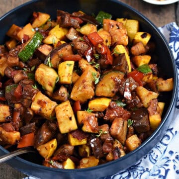 Chopped, cooked eggplant, squash, tomatoes, and red bell pepper in a bowl.
